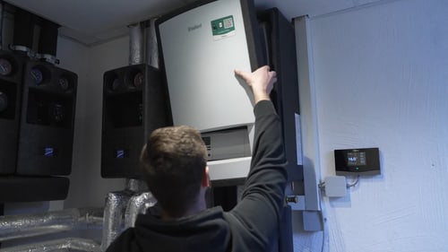 Ein Techniker montiert eine Vaillant-Wärmepumpe an einer grauen Wand in einem Technikraum.